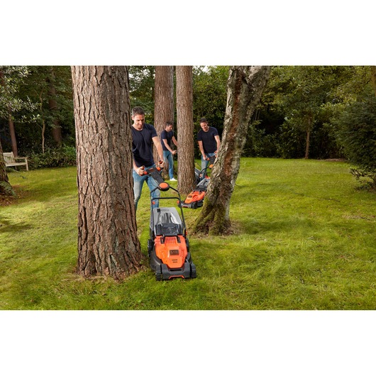 BLACKDECKER BEMW461ES lawn mower used by people mowing grass around trees in a garden.