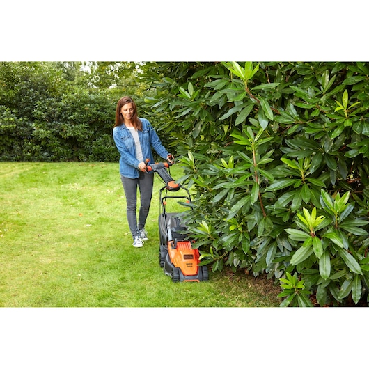 Photo of BLACKDECKER BEMW461ES lawn mower in use on grass near bushes outdoors.