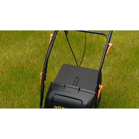 BLACKDECKER BEOEP320-QS lawn mower close-up showing black grass box and orange levers on green grass.