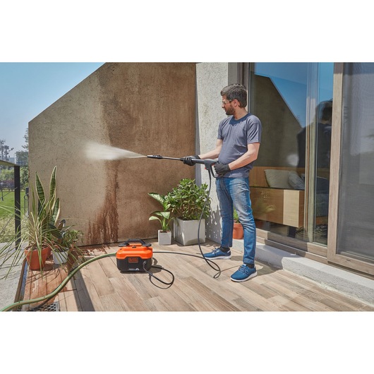 Photo of a person cleaning an outdoor wall with a BLACK+DECKER BEPW1300H pressure washer on a patio.