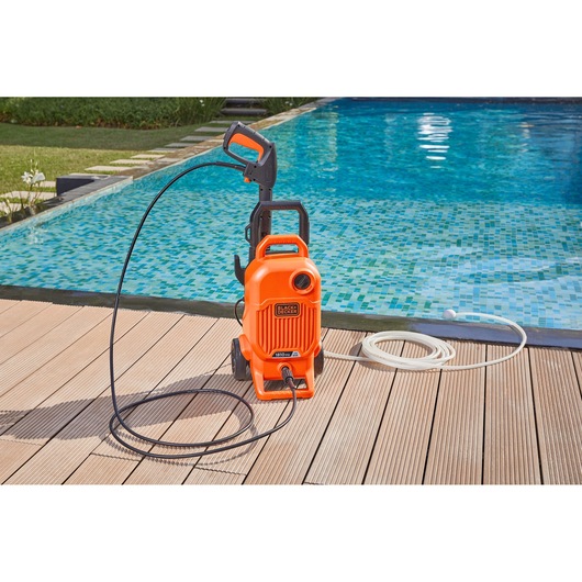 BLACK+DECKER BEPW1700 pressure washer with hose, orange, shown on poolside wooden deck.
