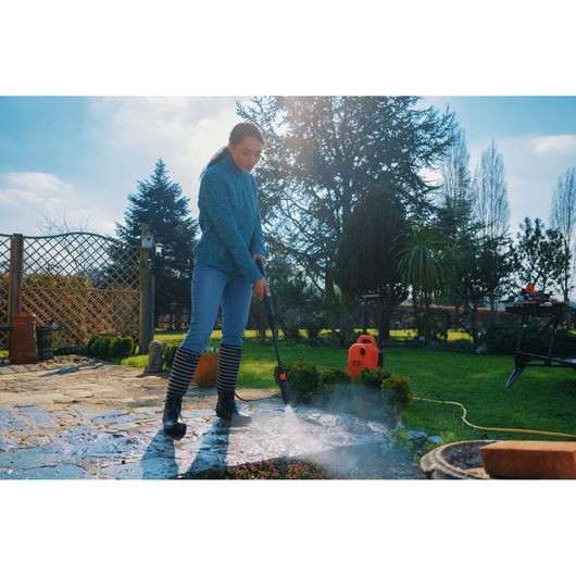 Photo of BLACKDECKER BEPW1700 pressure washer used outdoors to clean a stone patio, bright orange unit visible.