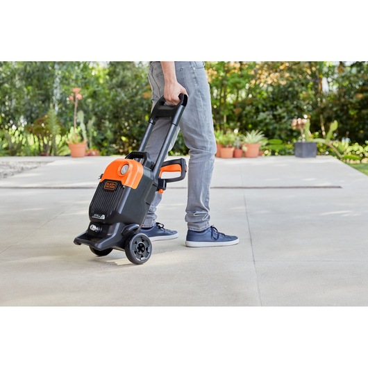 Photo of BLACKDECKER BEPW2000 pressure washer being wheeled outdoors by person, showing handle and wheels.
