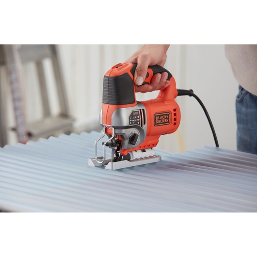 BLACK+DECKER BES610K jigsaw in use cutting corrugated metal, photography showing orange and black design.