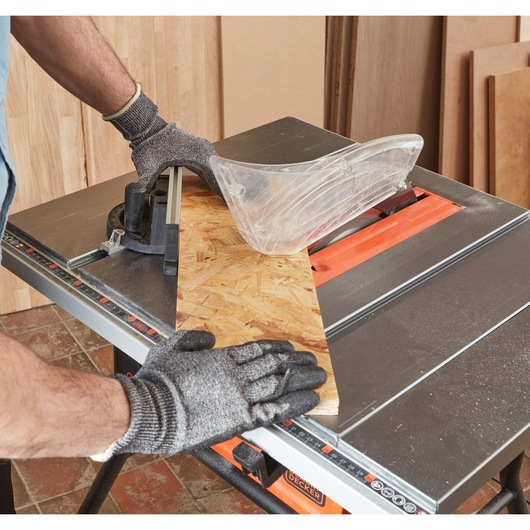 BLACKDECKER BES720 table saw front angle, cutting wood panel, gloves and safety guard visible.