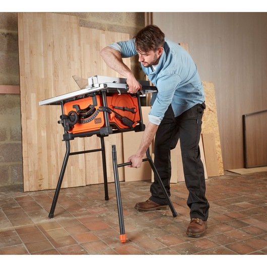 Photo of BLACKDECKER BES720 table saw being assembled by a person in a workshop setting, orange body, black legs.