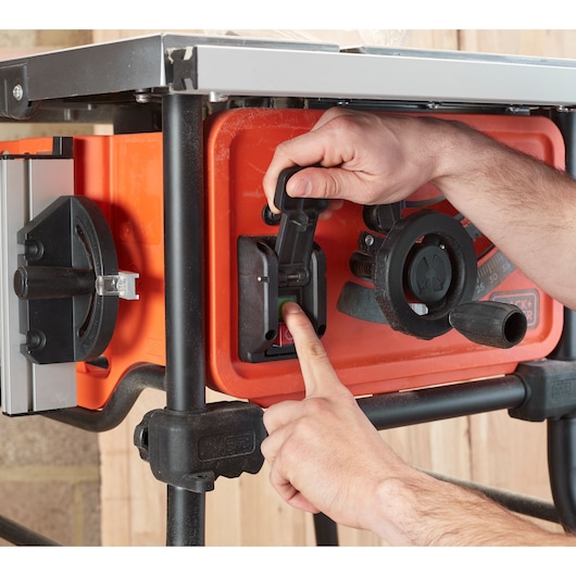Close-up of hands operating the BLACK+DECKER BES720 table saw power switch, orange body and black controls.