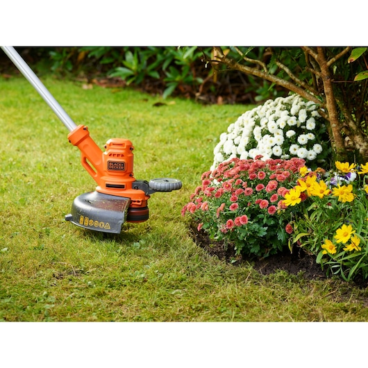 Photo of BLACK+DECKER BESTA530 grass trimmer in use edging lawn near colorful flower bed.