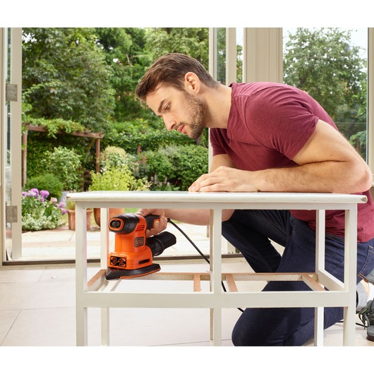 BLACKDECKER BEW200LSA sander used to smooth a white wooden table frame indoors near a window.