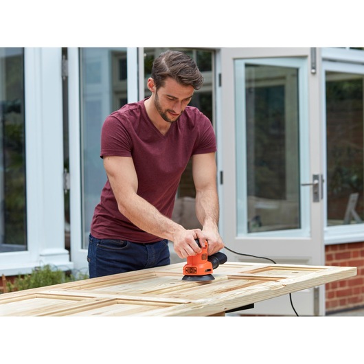 BLACKDECKER BEW200LSA sander in use on wooden door outdoors.