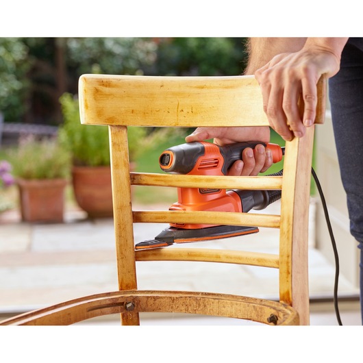 BLACKDECKER BEW200LSA detail sander used on wooden chair, orange and black handheld tool.