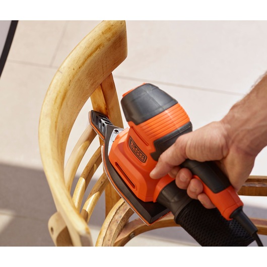 BLACKDECKER BEW200LSA detail sander used on a wooden chair, orange and black body, close-up.