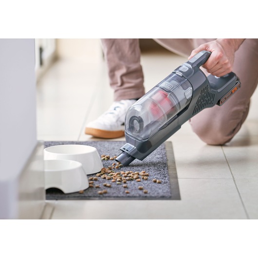 BLACKDECKER BHFEA18D1 handheld vacuum cleaning pet food on gray mat beside white bowls.