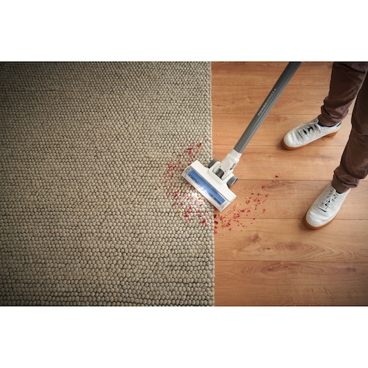 BLACKDECKER BHFEA420J cordless stick vacuum cleaning red debris from carpet and wood floor, top view.