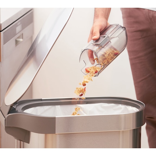 BLACKDECKER BHFEA420J vacuum dustbin being emptied into a kitchen trash can, close-up side view.
