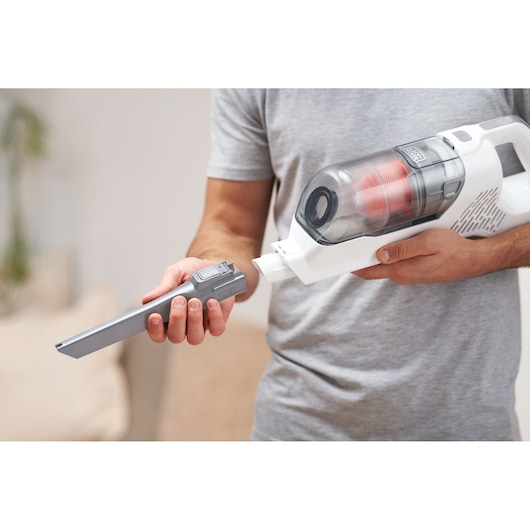 A person is holding a BLACK+DECKER cordless handheld vacuum cleaner and attaching a slim nozzle accessory.
