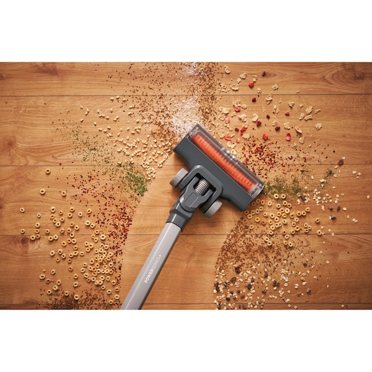 A BLACK+DECKER cordless vacuum cleaner cleaning scattered cereal and debris from a wooden floor.