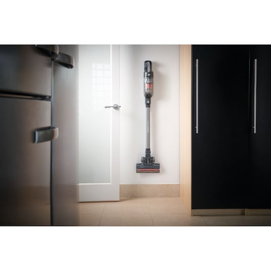 A BLACK+DECKER cordless stick vacuum cleaner model BHFEA520J mounted upright on a white wall in a modern kitchen.