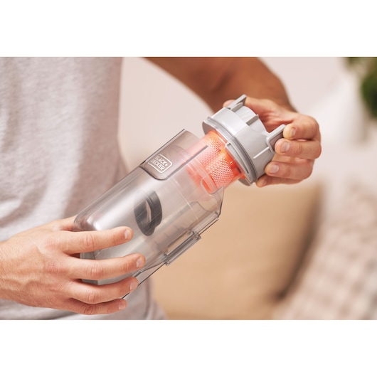 Close-up of a person holding and opening the dust container of a BLACK+DECKER cordless vacuum cleaner, showing the filter inside.