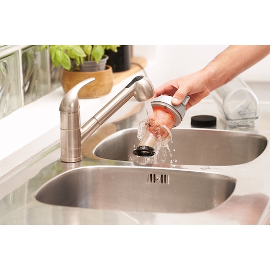 A person rinses a vacuum filter under running water in a kitchen sink, demonstrating easy cleaning for a BLACK+DECKER vacuum accessory.
