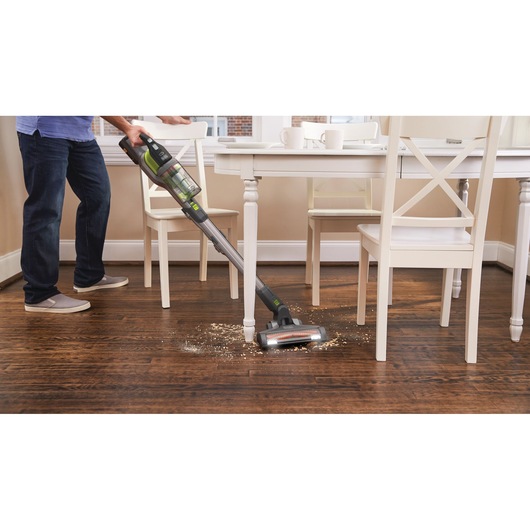 BLACKDECKER BHFEV362DA cordless stick vacuum cleaning debris on wooden floor near dining table.