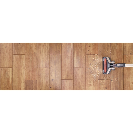 A BLACK+DECKER cordless vacuum cleaner is cleaning scattered debris from a wooden floor.