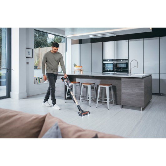 A person is removing the dust container from a BLACK+DECKER cordless vacuum cleaner in a home setting.