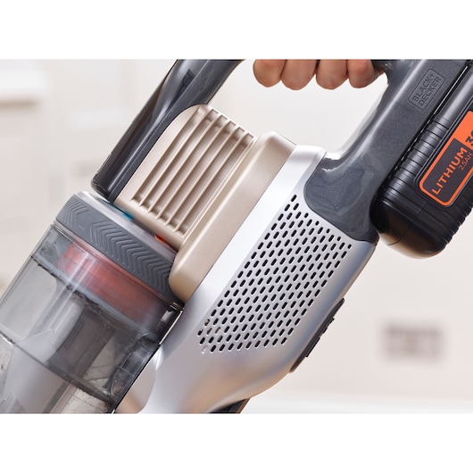 Close-up view of a BLACK+DECKER cordless vacuum cleaner being held by a person, showing details of the handle, battery, and dust container.