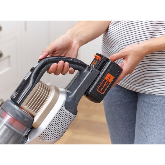Close-up of a person inserting a 36V lithium battery into a BLACK+DECKER cordless vacuum cleaner.