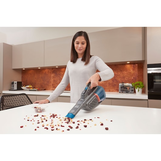 BLACKDECKER BHHV320J handheld vacuum cleaner being used to clean crumbs from a kitchen countertop.