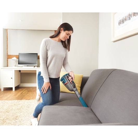 BLACKDECKER BHHV320J handheld vacuum cleaning a gray sofa in a modern living room.