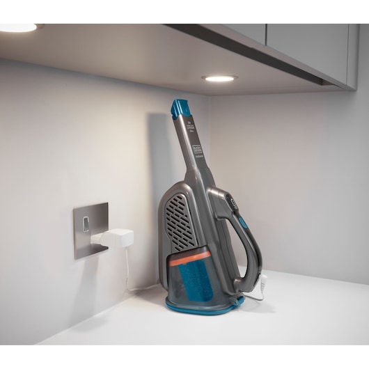 Photo of BLACKDECKER BHHV320J handheld vacuum charging on a white countertop under a cabinet.