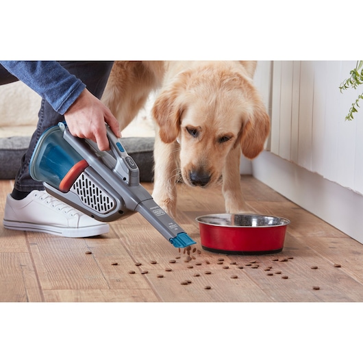 Photo of BLACKDECKER BHHV520BF handheld vacuum cleaning pet food near a red bowl on wood floor.