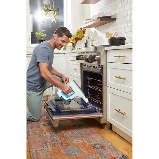 BLACKDECKER BHSM15FX08 steam cleaner used on oven door in modern kitchen setting.