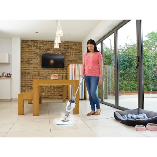 BLACKDECKER BHSM1615DSG steam mop cleaning tiled floor in modern kitchen next to wooden table and pet bed.