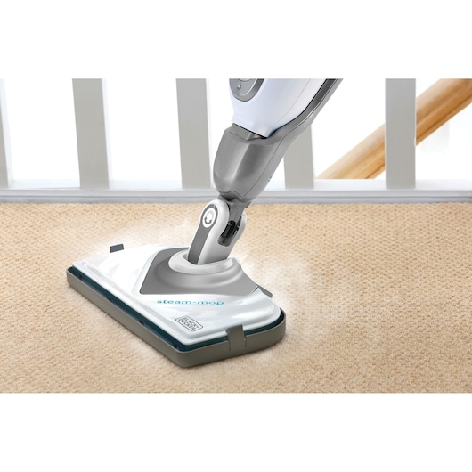 A BLACK+DECKER steam mop cleaning a light-colored carpet, showing steam coming from the mop head.
