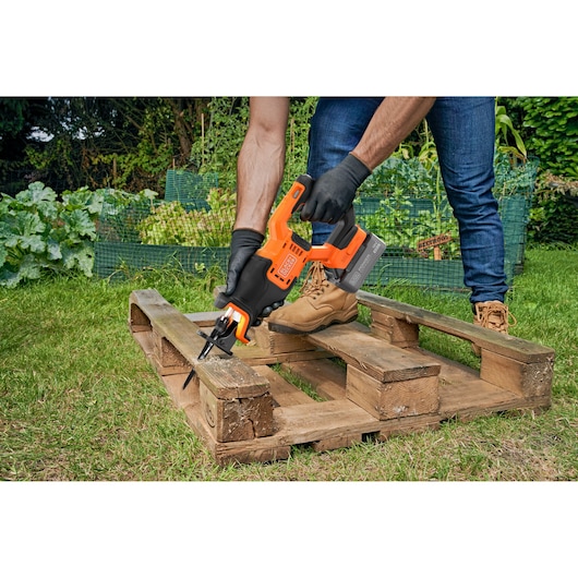 BLACK+DECKER BLCR78M1 cordless reciprocating saw in use, cutting a wooden pallet outdoors, close-up view.