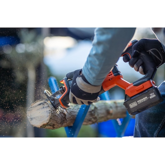 BLACKDECKER BLCR78M1 cordless saw used to cut wood outdoors, close-up of gloved hands in action.