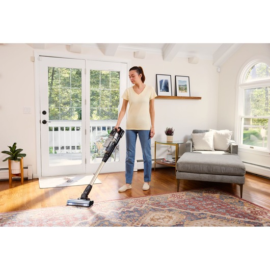 BLACKDECKER BSV525BLP cordless stick vacuum in use on hardwood and rug in bright living room.