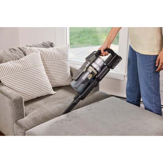 BLACKDECKER BSV525BLP cordless stick vacuum cleaning a sofa, handheld mode with crevice tool.