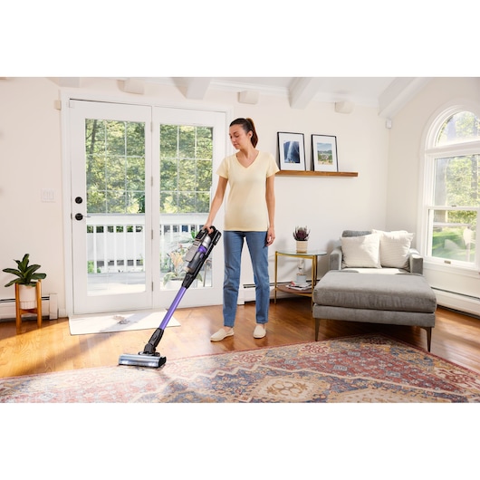 BLACKDECKER BSV525BRP cordless stick vacuum with purple wand being used on hardwood and carpet in a living room.