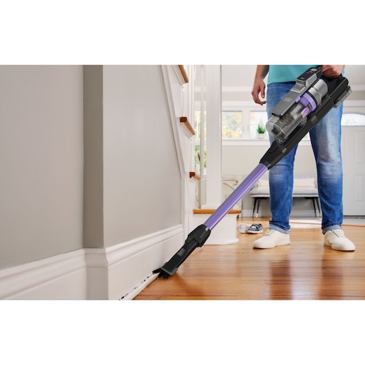 BLACKDECKER BSV525BRP cordless stick vacuum, purple and black, cleaning floor edges in a home.
