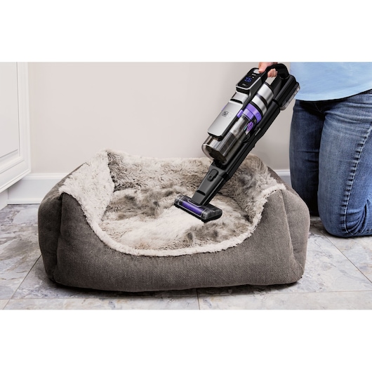 BLACKDECKER BSV525BRP handheld vacuum cleaning a gray furry pet bed, indoor setting, side angle.