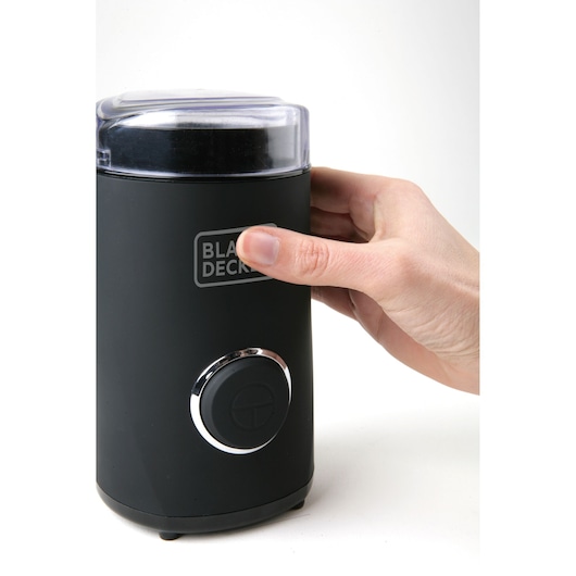 BLACKDECKER BXCG150E coffee grinder with black matte finish and transparent lid, side angle, hand pressing button