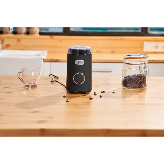 BLACKDECKER BXCG150E coffee grinder in black, with glass jar and cup on wooden kitchen table.
