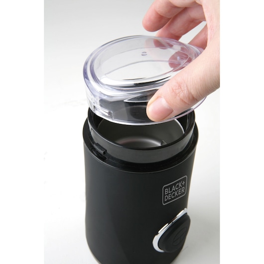 BLACK+DECKER BXCG150E coffee grinder with clear lid, hand removing lid, photographed from above.