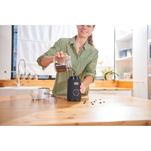BLACKDECKER BXCG150E coffee grinder in use, coffee beans being poured in, kitchen setting.