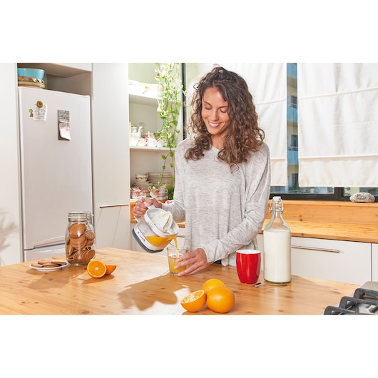 BLACKDECKER BXCJ25E citrus juicer on kitchen table pouring juice into glass, oranges and milk nearby.