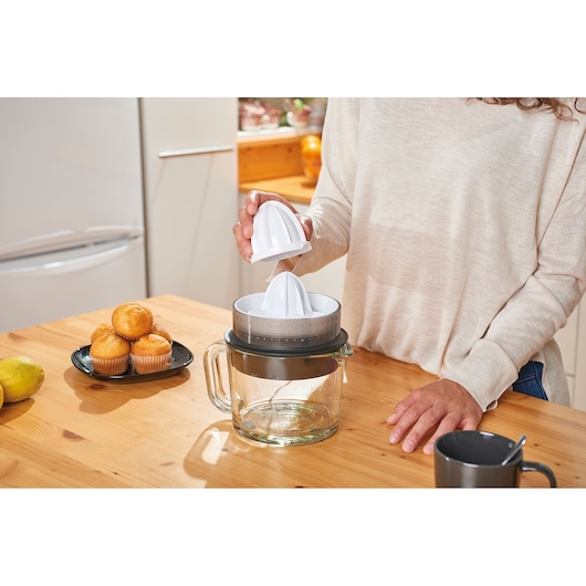 BLACKDECKER BXCJ30E citrus juicer with glass container on wooden table, person preparing parts.