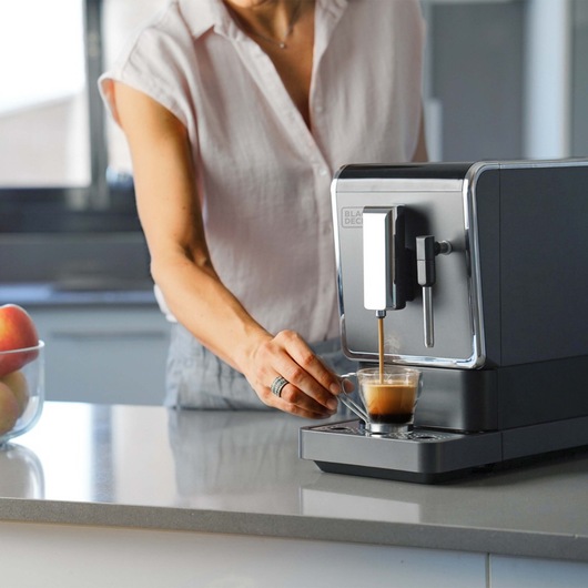BLACKDECKER BXCO1470E coffee machine brewing espresso in kitchen with a person holding a glass cup.
